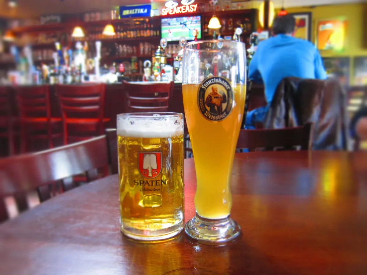 A stein of golden lager and a glass of cloudy wheat beer on the bar at Bistro Gambrinus